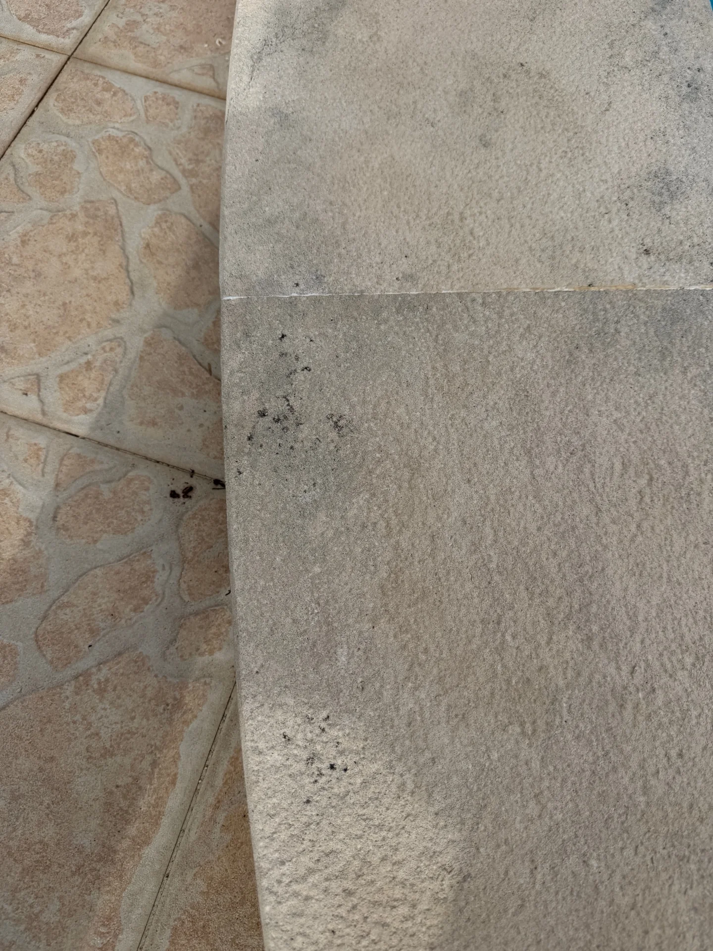 Vista aproximada de uma borda de piscina clara e áspera, com pontos escuros e uma junta
