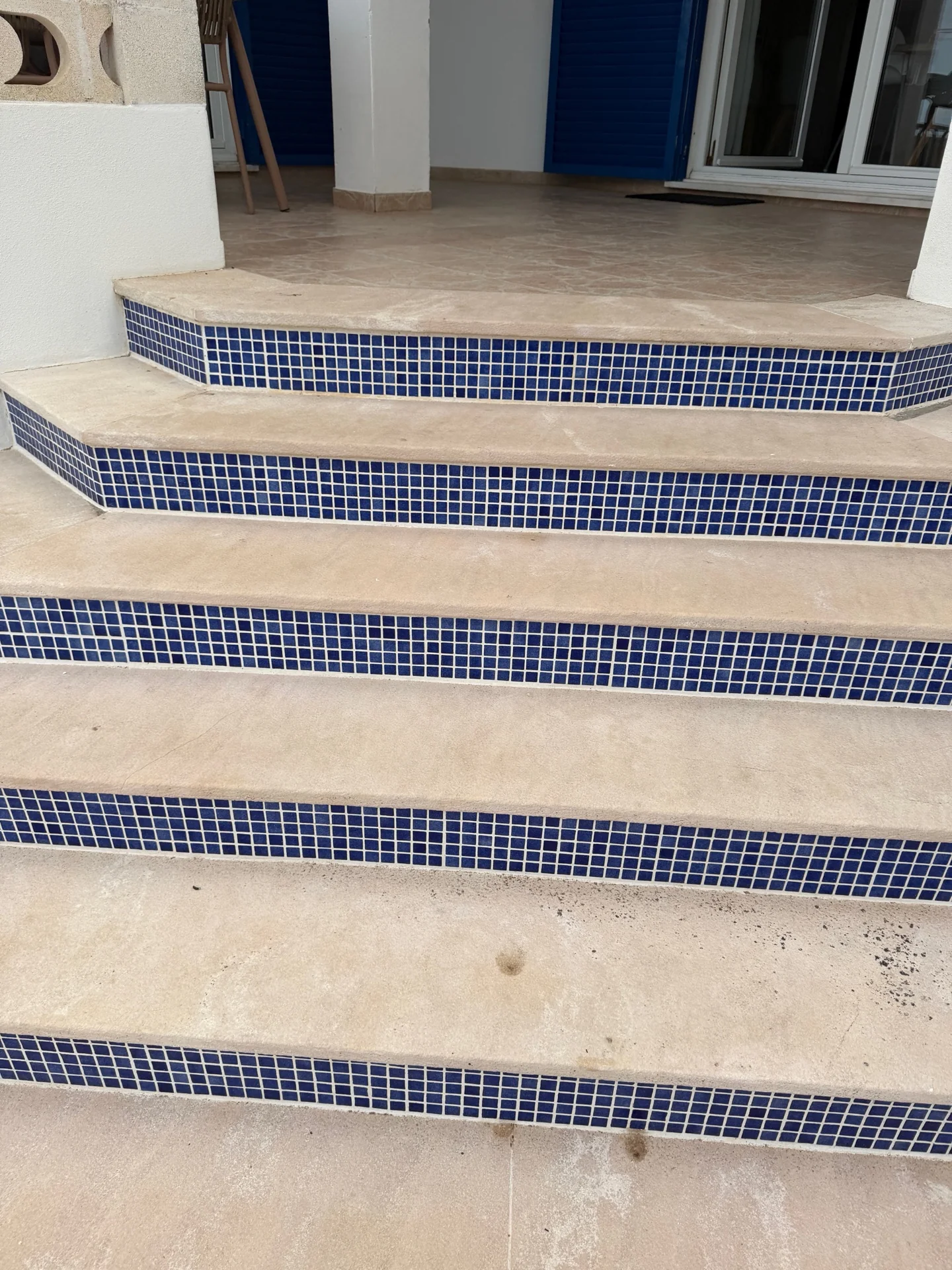 Escada exterior diante de um terraço, com degraus claros e mosaico azul nos espelhos